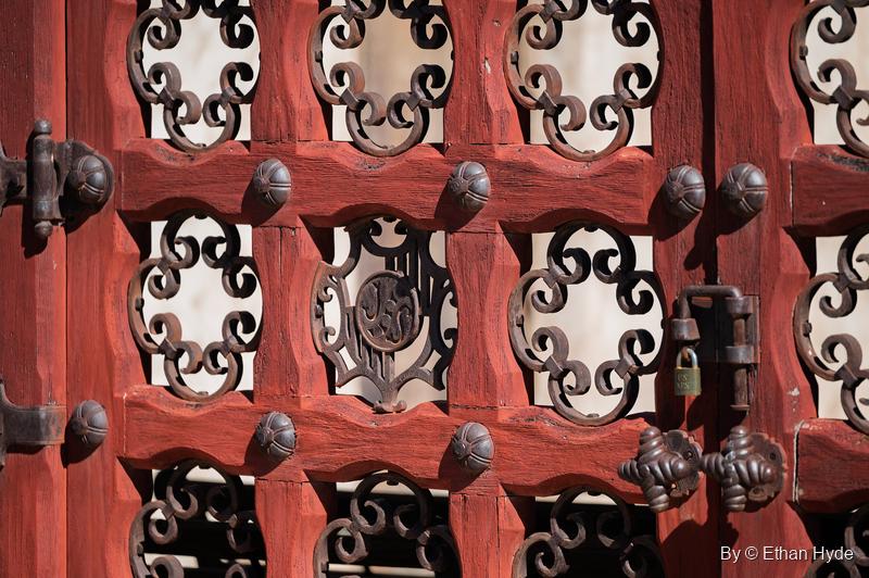 Close-up of the red courtyard gates at Scotty's Castle: iron scrollwork, studded rails, a padlock and a monogram panel.
