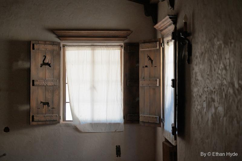 Light through a curtained window inside Scotty's Castle, flanked by wooden shutters cut out with desert animal silhouettes.