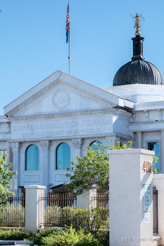 Front of the Supreme Court of Nevada building: a white pediment, arched windows, a dome with Lady Justice and an American flag.