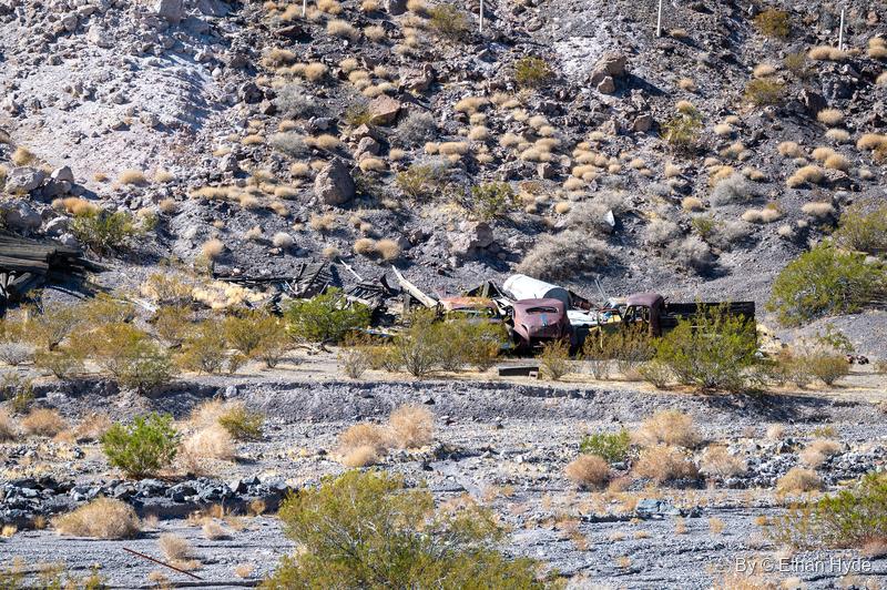 Rusted vintage cars and scrap lumber piled at the foot of a rocky hillside in Tie Canyon near Scotty's Castle.