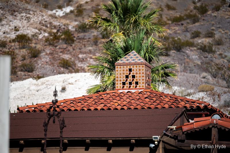 A patterned tile chimney cap on a red tile roof at Scotty's Castle, a palm and desert hillside behind.