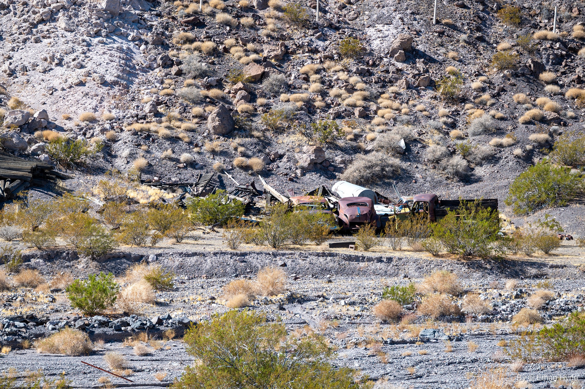 Rusted vintage cars and scrap lumber piled at the foot of a rocky hillside in Tie Canyon near Scotty's Castle.