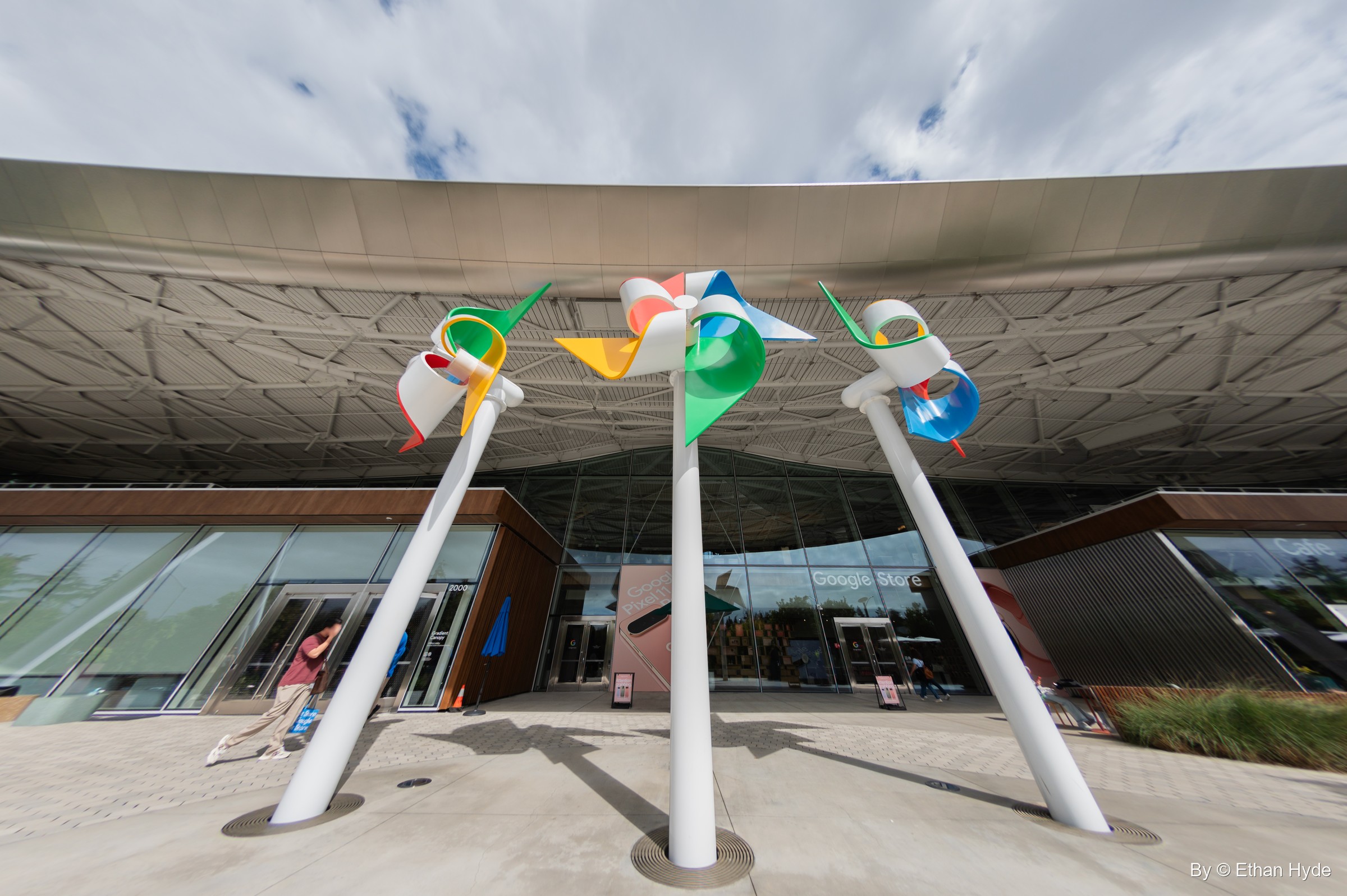 Wide view of colorful pinwheel sculptures under the scalloped steel canopy roof of Google's Gradient Canopy building.